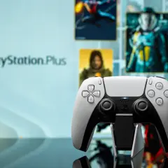 Biały kontroler DualSense na tle ekranu z logo PlayStation Plus i okładkami gier. Idealny do grania w gry z oferty PS Plus marzec.