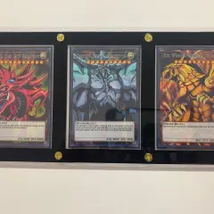 Trzy karty Yu-Gi-Oh! w ramce: Slifer the Sky Dragon, Obelisk the Tormentor i The Winged Dragon of Ra.