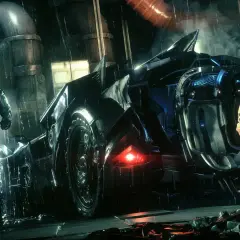 Batman w deszczu przy Batmobilu, gotowy do akcji w Arkham City. Obok niego klęczy mężczyzna w pomarańczowym kombinezonie.