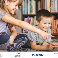 Dzieci z uśmiechem odkrywają świat gier cyfrowych na laptopie, siedząc na dywanie przed regałem pełnym książek.