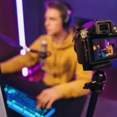 Kamerka do streamowania rejestruje młodego gracza w żółtej bluzie, otoczonego neonowym światłem.