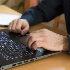 Mężczyzna pracuje na laptopie z podświetlaną klawiaturą, szukając informacji, jak zwiększyć wydajność laptopa w grach.
