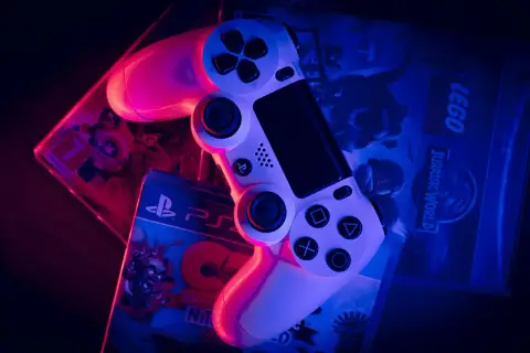 Biały kontroler PlayStation na pudełkach gier: LEGO Jurassic World i Crash Bandicoot. To wersja gry pudełkowa, którą można postawić na półce.