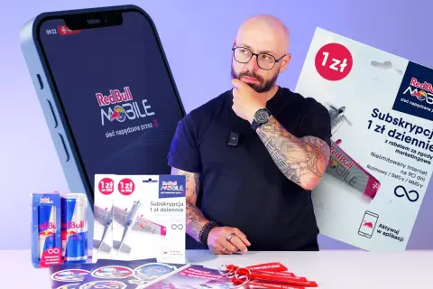 Mężczyzna z tatuażami zastanawia się nad ofertą Red Bull MOBILE. Na stole leżą puszki Red Bull, karty SIM i gadżety.