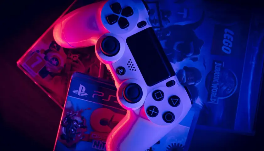 Biały kontroler PlayStation na pudełkach gier: LEGO Jurassic World i Crash Bandicoot. To wersja gry pudełkowa, którą można postawić na półce.