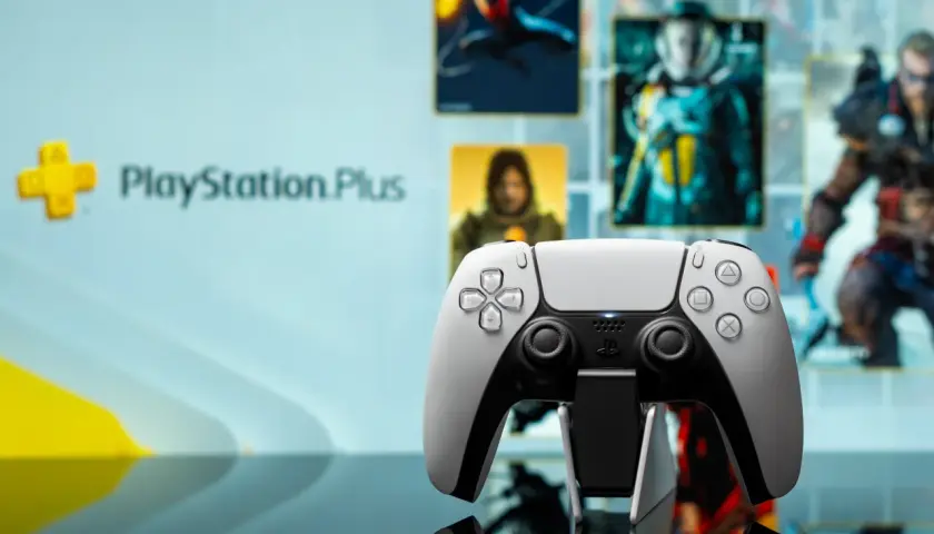 Biały kontroler DualSense na tle ekranu z logo PlayStation Plus i okładkami gier. Idealny do grania w gry z oferty PS Plus marzec.