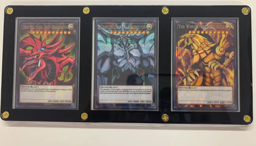 Trzy karty Yu-Gi-Oh! w ramce: Slifer the Sky Dragon, Obelisk the Tormentor i The Winged Dragon of Ra.