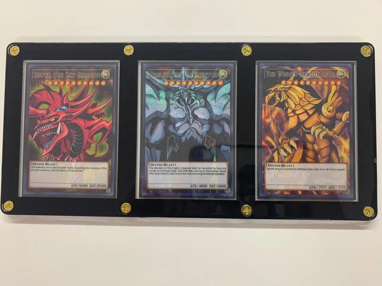 Trzy karty Yu-Gi-Oh! w ramce: Slifer the Sky Dragon, Obelisk the Tormentor i The Winged Dragon of Ra.