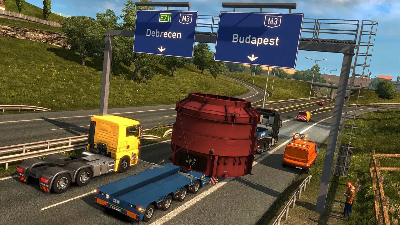 Transport ciężkiej maszyny w Euro Truck Simulator 3. Ciężarówka z żółtą kabiną i niebieską naczepą przewozi ogromny czerwony element.