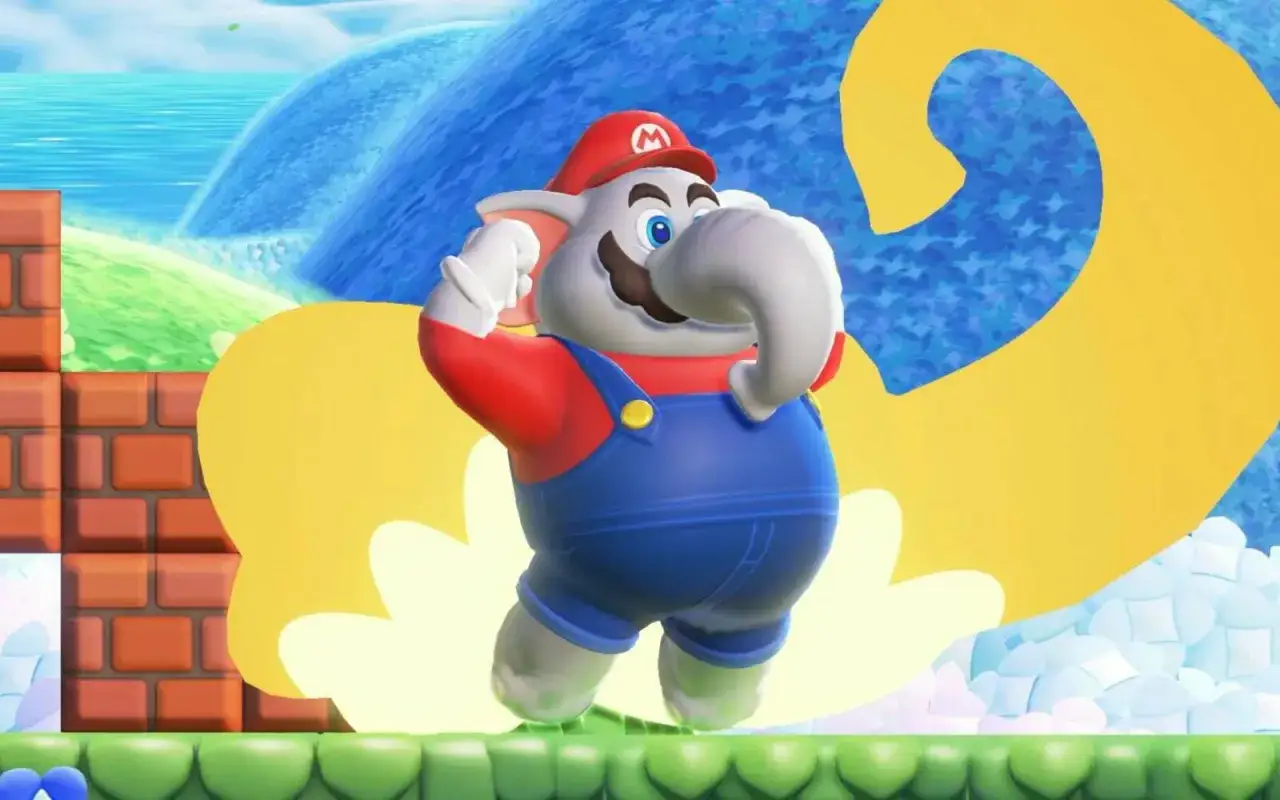 Słoń Mario w niebieskich ogrodniczkach, bohater gry Mario Bros Wonder, radośnie podnosi trąbę na tle wodospadu i żółtego znaku.