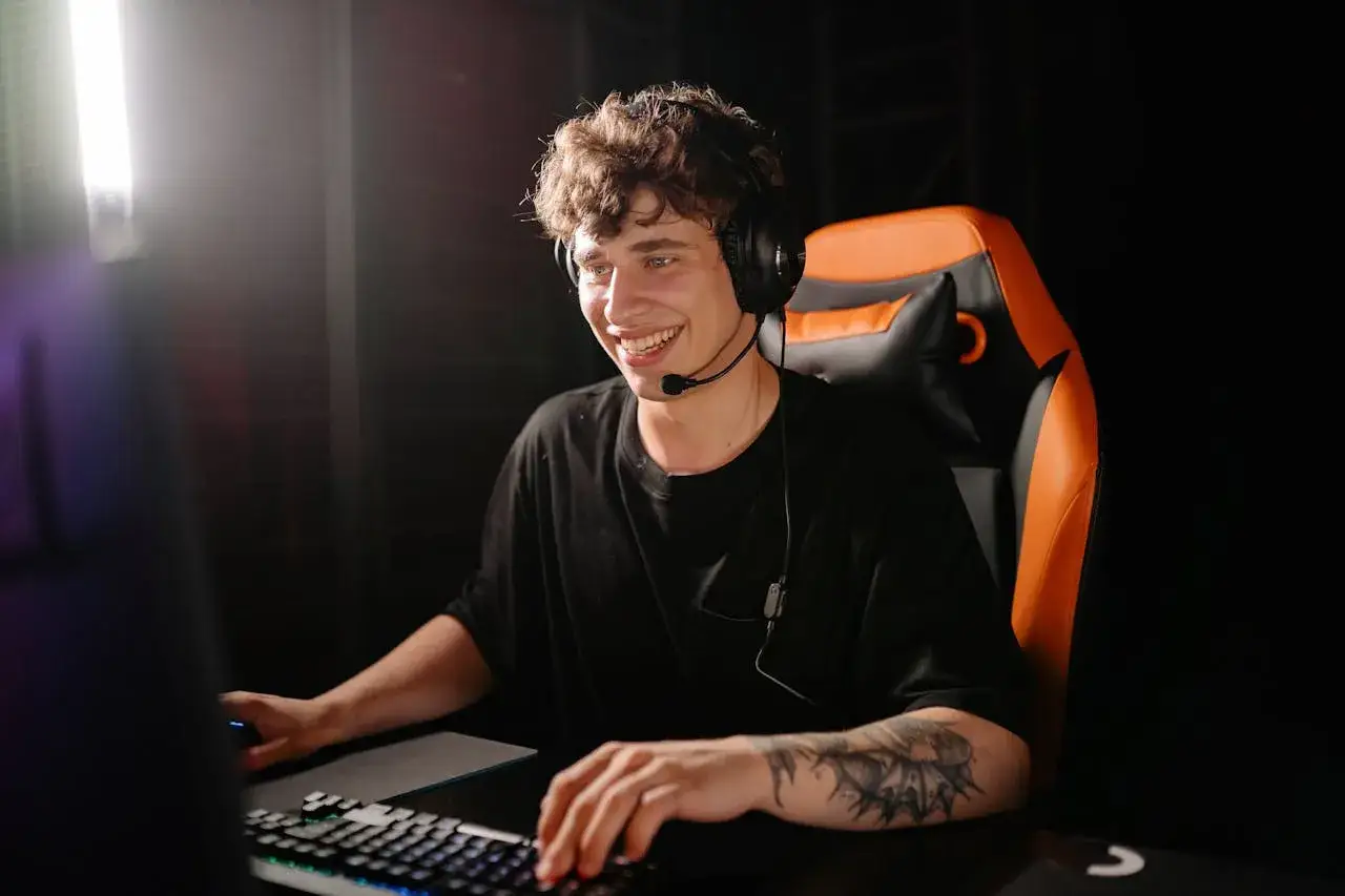 Uśmiechnięty gracz w słuchawkach z mikrofonem, siedzący na gamingowym fotelu. Dowiedz się, jak zwiększyć FPS na laptopie, by cieszyć się płynną rozgrywką.