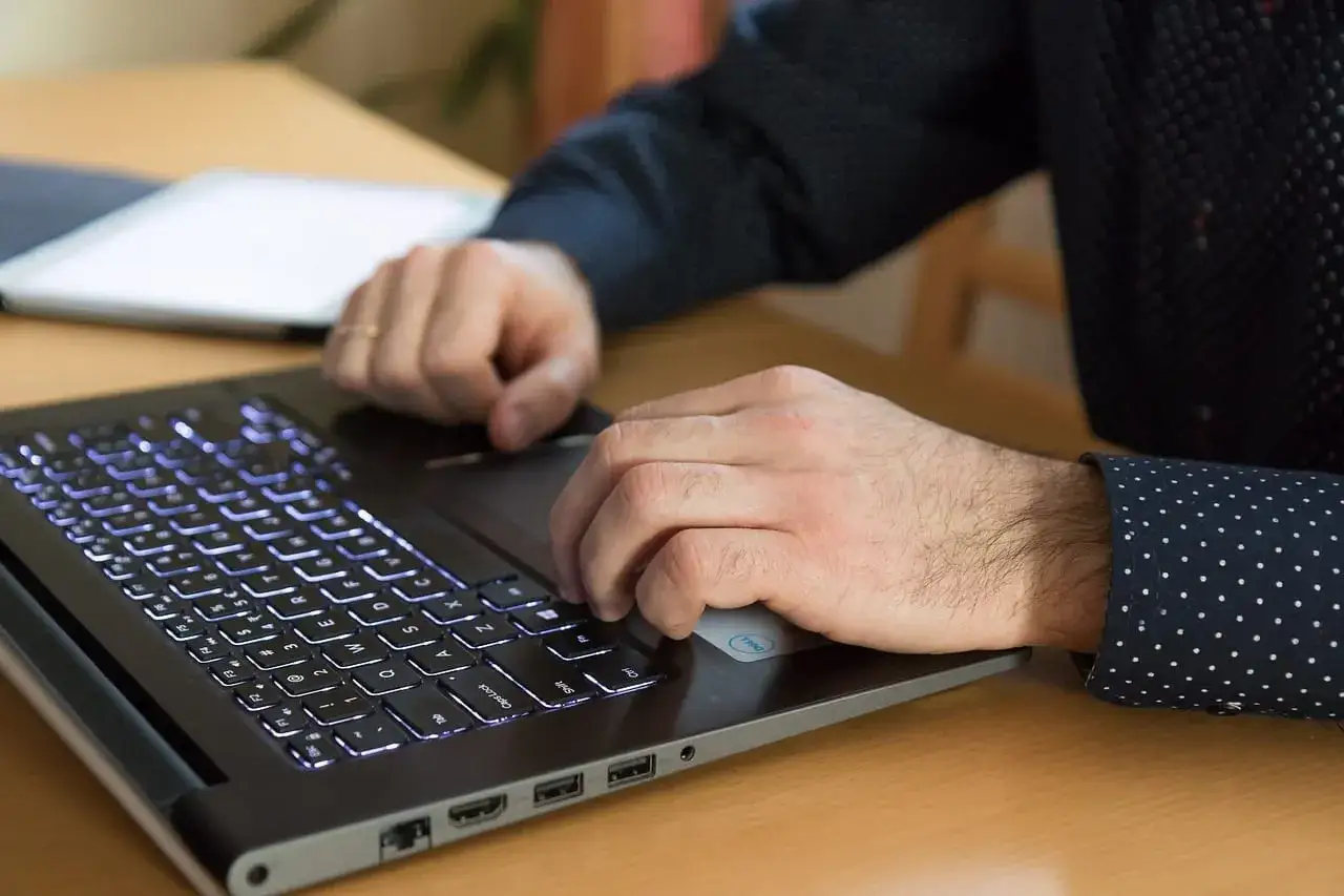 Mężczyzna pisze na laptopie z podświetlaną klawiaturą, szukając porad, jak zwiększyć fps na laptopie.