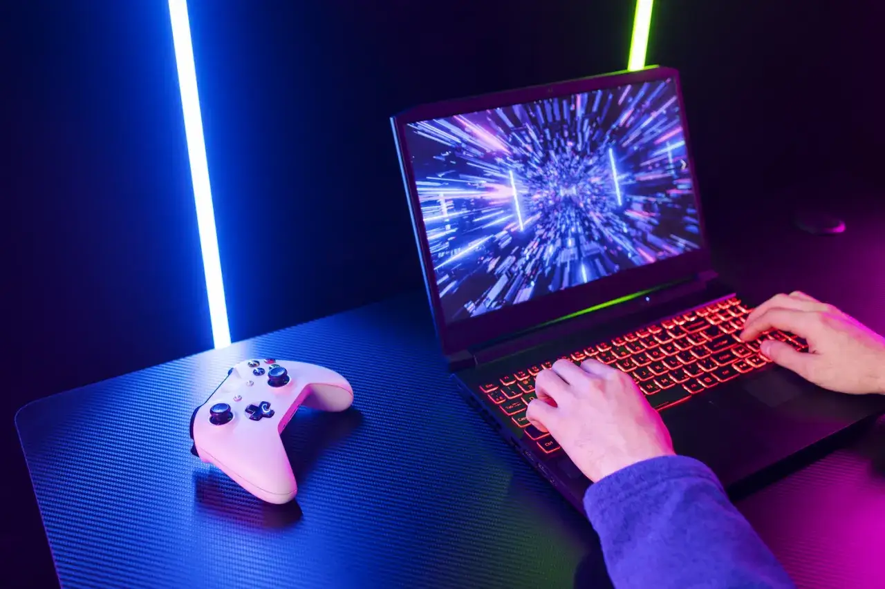 Gracz gra na podświetlanym laptopie, obok leży biały kontroler. Dowiedz się, jak zwiększyć wydajność laptopa w grach, by cieszyć się płynną rozgrywką.