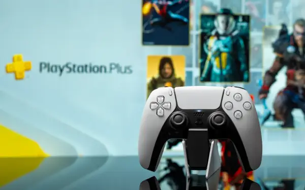 Biały kontroler DualSense na tle ekranu z logo PlayStation Plus i okładkami gier. Idealny do grania w gry z oferty PS Plus marzec.